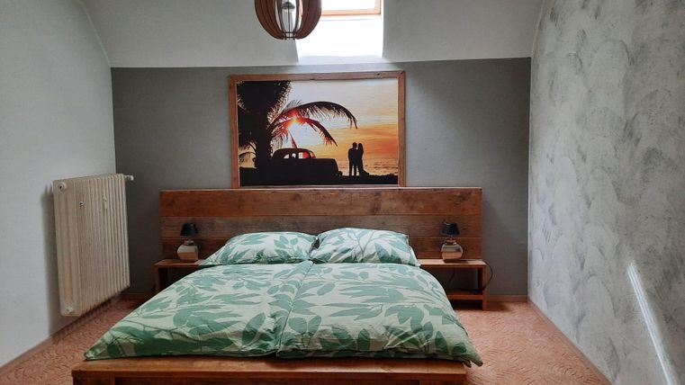 Ein gemütliches Schlafzimmer mit einem großen Bett und grünen Kissen. An der Wand hängt ein Bild mit einer Palmenlandschaft und einem Paar.