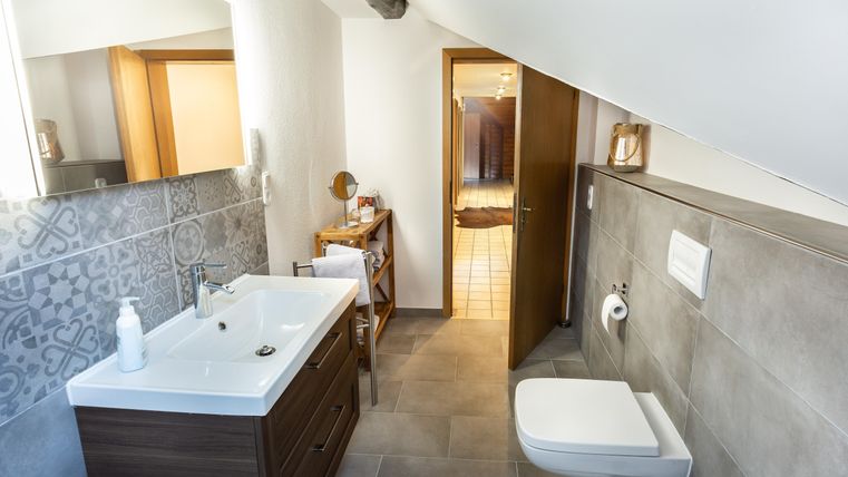 A modern bathroom with a sink, wooden cabinets, and a toilet. The walls are designed with tiles in neutral colors.