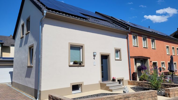 Ein modernes Einfamilienhaus mit Solarpanelen auf dem Dach. Die Fassade ist hell und freundlich, umgeben von einer gepflegten Steinanlage.
