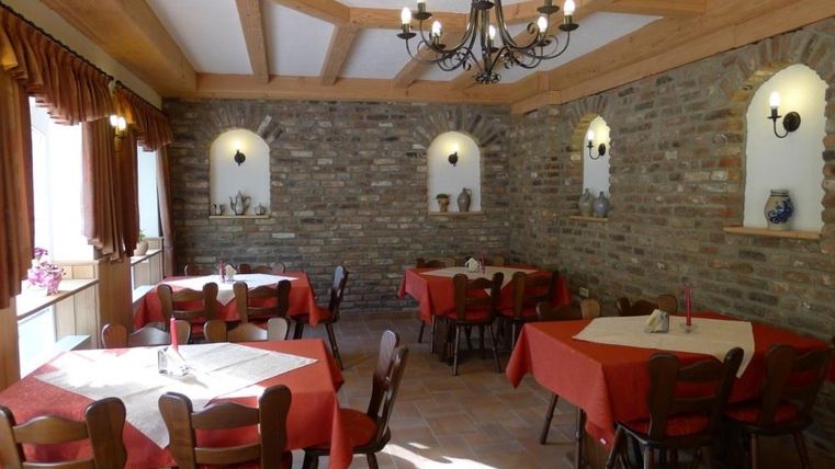 A cozy restaurant with red-covered tables and a warm stone wall design. The room has large windows and stylish lighting.