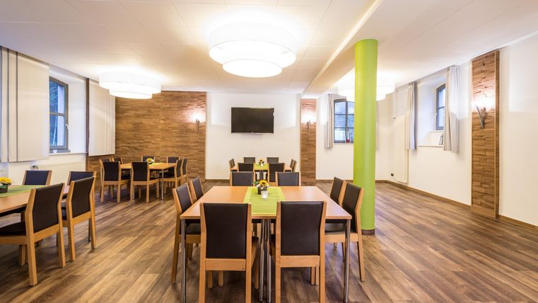 Een moderne vergaderruimte met een houten vloer en grote ramen. De tafels zijn netjes gerangschikt en versierd met groene tafelkleden.