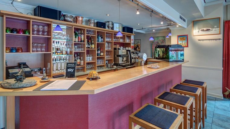 Un bar moderne avec des étagères en bois et un comptoir. À l'arrière-plan, diverses boissons et un petit paysage aquatique sont visibles.