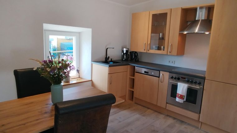 Een moderne keuken met houten kasten en roestvrijstalen apparaten. Op tafel staan verse bloemen en een raam biedt daglicht.