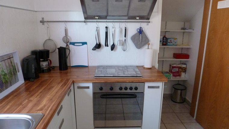 Eine moderne Küche mit Holzarbeitsplatte und verschiedenen Kochutensilien. Im Hintergrund ist ein offenes Regal zu sehen.