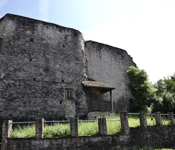 Ruine der Burg Bettingen mit massiven Steinmauern, umgeben von gr&uuml;ner Vegetation unter blauem Himmel., &copy; TI Bitburger Land