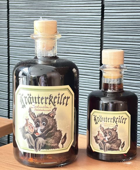 Zwei Flaschen Kräuterlikör stehen auf einem Tisch. Die Flaschen haben ein charakteristisches Etikett mit einem abgebildeten Wildschwein.