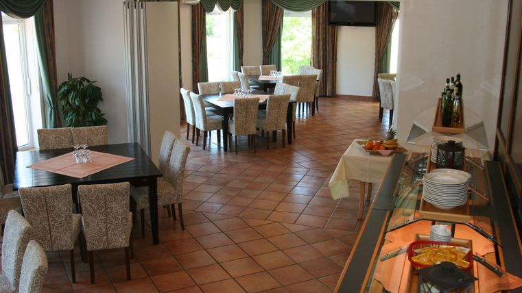 Een elegante eetzaal met tafels en stoelen. Aan één zijde is er een buffet met verschillende gerechten.