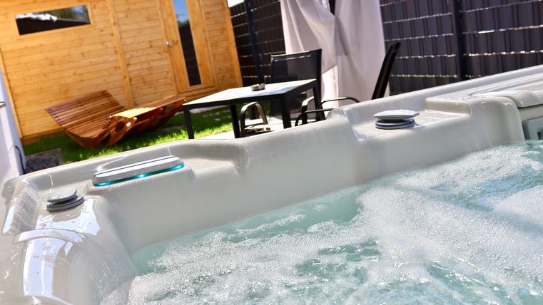 Ein Whirlpool mit sprudelndem Wasser ist im Vordergrund zu sehen. Im Hintergrund steht ein schöner Garten mit einem Holzhaus und einem Tisch.