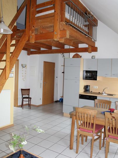 Een lichte woning met een open indeling, die een houten trap en een eetgedeelte toont. De keuken is modern en goed uitgerust.