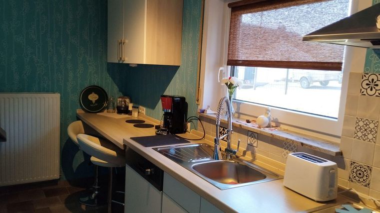 Eine moderne Küche mit blauer Wandtapete und einer praktischen Arbeitsfläche. Es gibt eine Spüle, ein Toaster und eine gemütliche Bar mit Stühlen.