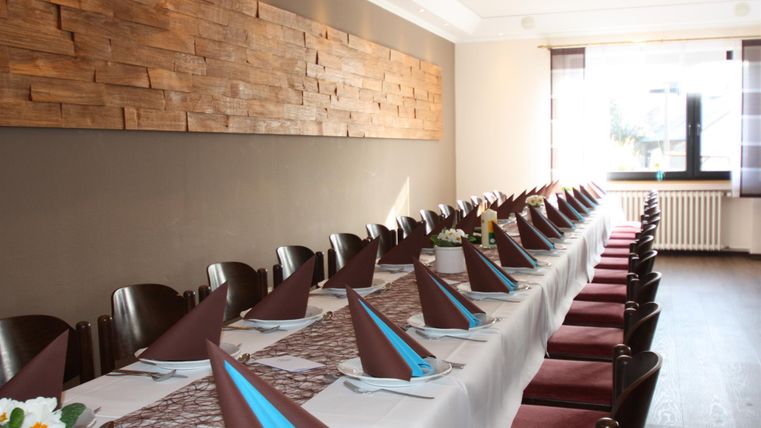 Une salle à manger élégante avec une longue table, dressée pour un événement. Les nappes sont décorées avec des serviettes marron et bleues, et un mur en bois crée une ambiance agréable.