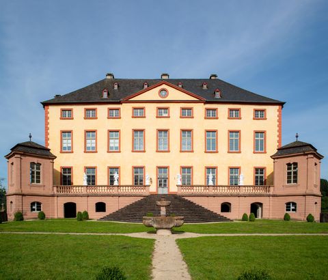 Ein prächtiges Gebäude mit einer symmetrischen Fassade und großen Fenstern. Die Umgebung ist von grünem Rasen und einem klaren Himmel umgeben.