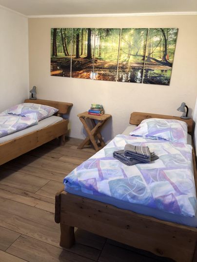 A cozy sleeping room with two wooden beds. A beautiful picture of a forest hangs on the wall, and on the beds, there are towels.