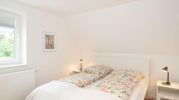 Une chambre claire avec un lit double et des couvertures colorées.
Sur le mur, il y a une image, et il y a deux lampes de chevet.  