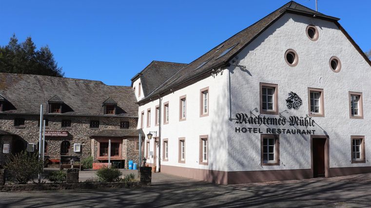 A charming hotel building with a restaurant. The facade is white, and the sky is clear and blue.