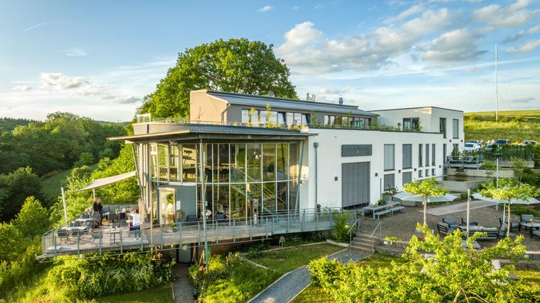 Un bâtiment moderne avec de grandes fenêtres se trouve dans un environnement verdoyant. La terrasse est idéale pour des moments de détente en plein air.