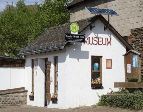 Ein kleines, weißes Museumgebäude mit einem Schild oben. Es gibt einen Bus-Halteplatz neben dem Museum.