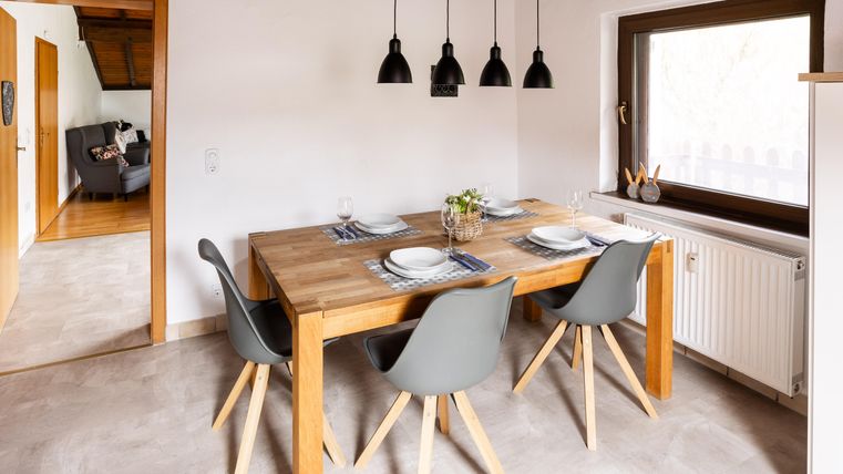 A bright dining room with a wooden tray and six modern chairs. The pendant lights and the large window create an inviting atmosphere.