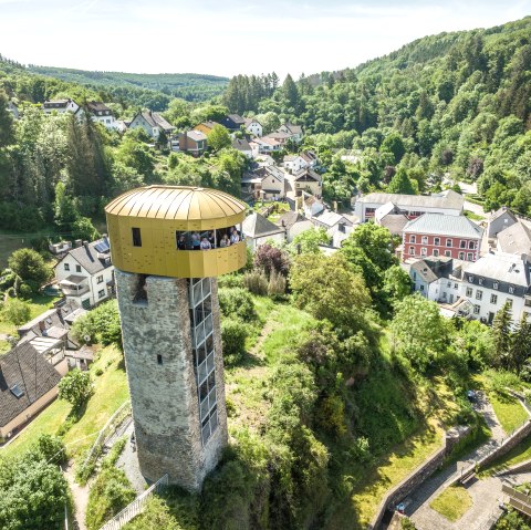 Ein Turm mit goldener Aussichtsplattform überblickt eine grüne Landschaft und eine kleine Siedlung. Im Hintergrund sind Wälder zu sehen., © Eifel Tourismus GmbH, Dominik Ketz