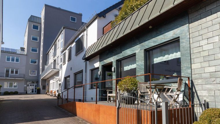 Ein modernes Gebäude mit einer Glasfassade und einem begrünten Außenbereich. Die Architektur ist zeitgemäß und lädt zum Verweilen ein.