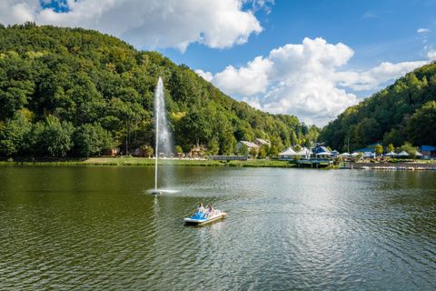 Un lac pittoresque avec une cascade et des collines verdoyantes en arrière-plan. Quelques personnes profitent d'une promenade en bateau sur les eaux calmes.