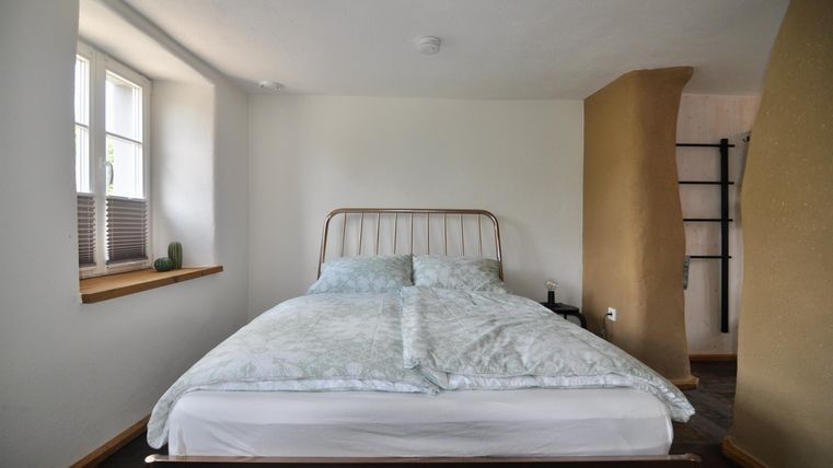 Ein einfaches Schlafzimmer mit einem Bett und hellen Wänden. Das Zimmer hat ein Fenster und eine gemütliche Atmosphäre.