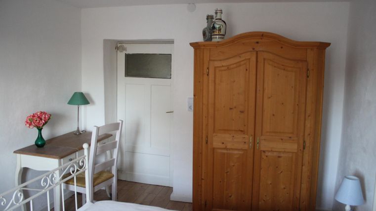 Ein gemütliches Schlafzimmer mit einem Holzschrank und einem kleinen Tisch. An der Wand steht eine Lampe und eine Vase mit Blumen.