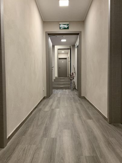 Ein heller Flur mit grauem Boden und weißen Wänden. Am Ende des Flurs sind mehrere Türen sichtbar.