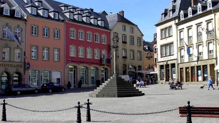 Un bel endroit avec des bâtiments colorés et une statue au centre. Il y a quelques personnes qui s'y trouvent et profitent du temps.