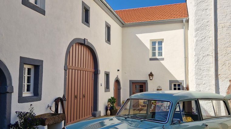 Een klassiek, mintgroen auto staat voor een charmant, licht gebouw. De lucht is helder en blauw, wat een uitnodigende sfeer creëert.