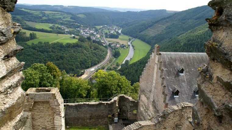 Un regard depuis une vieille ruine de château sur un paysage verdoyant. À l'arrière-plan, une rivière coule et suit le long de la colline.