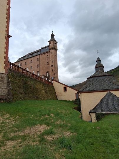 Un vieux château se dresse sur une colline, entouré d'une prairie verte. En arrière-plan, des nuages gris sont visibles dans le ciel.