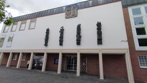 Ein modernes Gebäude mit einer klaren Fassade und mehreren Skulpturen an der Wand. Über dem Eingang befindet sich ein Wappen.