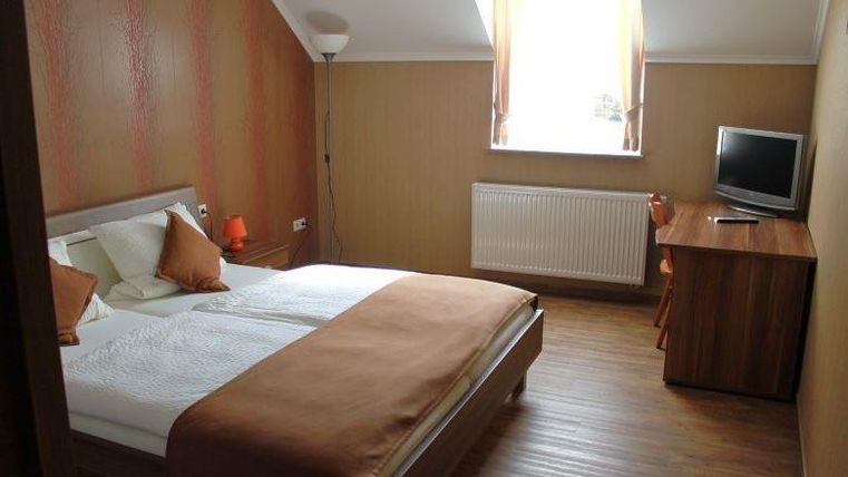 Ein helles und modernes Schlafzimmer mit einem Doppelbett und gemütlichen Kissen. Es gibt einen Schreibtisch, einen Fernseher und ein großes Fenster für viel Tageslicht.