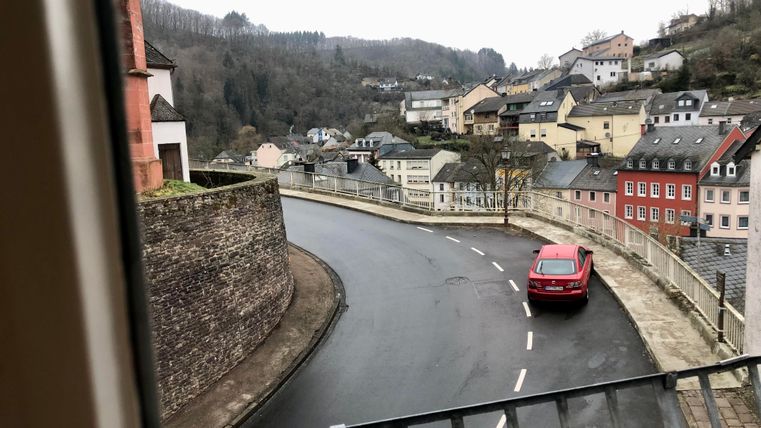 A winding road in a quiet town. In the background, rising hills and colorful houses can be seen.