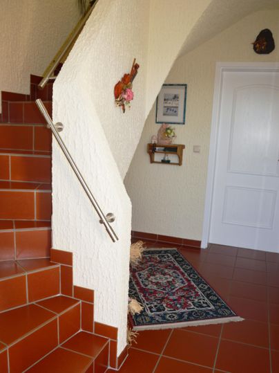 An inviting entrance area with a staircase and a beautiful carpet. Some decorative elements hang on the wall.