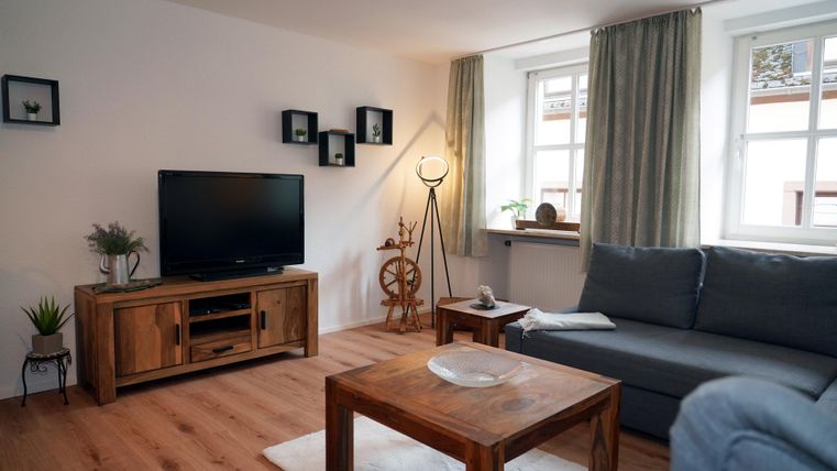 Een moderne woonkamer met een grijze bank, een houten tafel en een televisie. De televisie heeft een HDMI-aansluiting voor uw entertainmentsysteem (bijv. FireTV Stick, PlayStation, enz.).