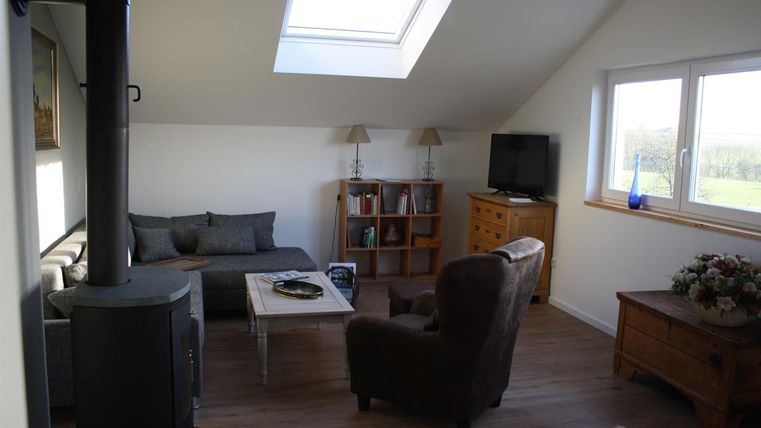 Ein gemütlicher Wohnbereich mit einem Sofa und zwei Sesseln. Große Fenster sorgen für viel Tageslicht.