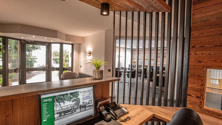 Une réception moderne avec un design en bois. Grâce aux grandes fenêtres, beaucoup de lumière naturelle est visible, et à l'arrière-plan, il y a d'autres zones de sièges.