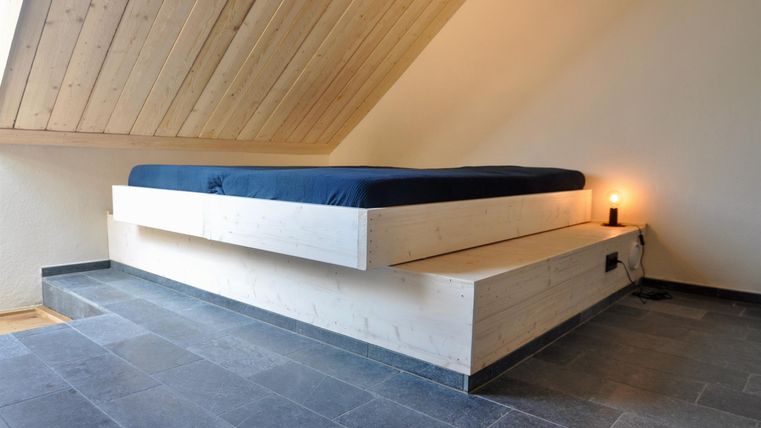 Ein modernes Schlafzimmer mit einem schlichten Bett und einer Holzdecke. Der Raum hat einen minimalistischen Stil und eine ruhige Atmosphäre.