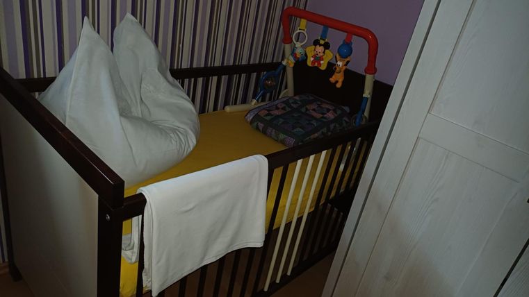 Ein Kinderbett mit gelber Matratze und Kissen. An der Seite hängen bunte Spielzeuge.