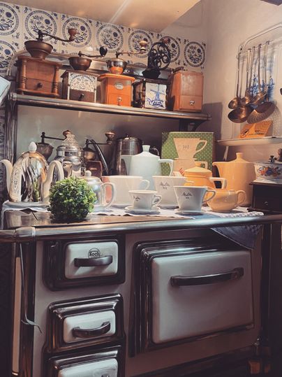 Une cuisine nostalgique avec une cuisinière classique et de la jolie vaisselle. Au-dessus du plan de travail, différents appareils de cuisine et décorations pendent.