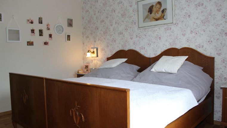 Ein gemütliches Schlafzimmer mit einem großen Holzbett und weißen Betttüchern. An der Wand hängen Bilder und eine Uhr, die eine einladende Atmosphäre schaffen.