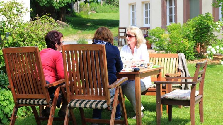 Eine gemütliche Gartenrunde mit drei Frauen am Tisch. Sie genießen Getränke und die schöne Umgebung.