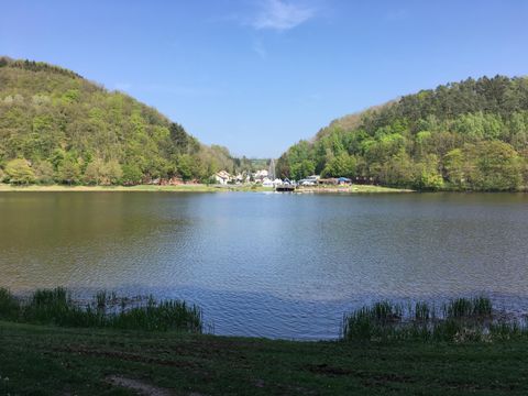Een rustige meer omringd door zachte heuvels en groene oeverbeplanting. De lucht is helder en blauw, ideaal voor een ontspannen dag in de natuur.