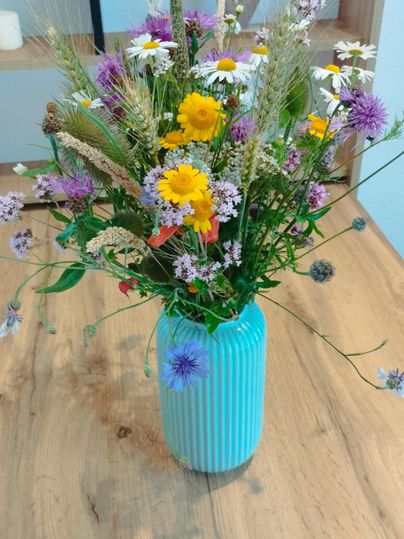 Een kleurrijk boeket met verschillende wilde bloemen in een blauwe vaas. Het boeket staat op een houten tafel.