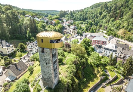 Ein Turm mit goldener Aussichtsplattform &uuml;berblickt eine gr&uuml;ne Landschaft und eine kleine Siedlung. Im Hintergrund sind W&auml;lder zu sehen., &copy; Eifel Tourismus GmbH, Dominik Ketz