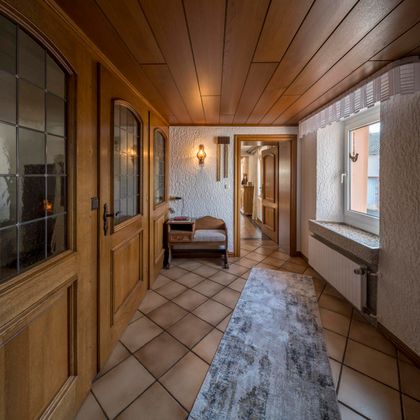 Ein einladender Flur mit Holzverkleidung und einem hellem Teppich. Das Licht durch die Fenster schafft eine warme Atmosphäre.