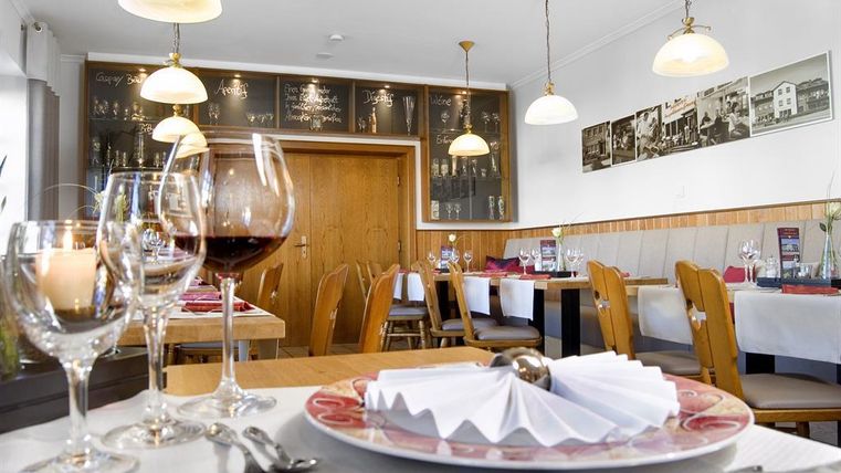 Een gezellig restaurant met elegante tafellakens en feestelijk gedekte tafels. Op de achtergrond zijn er schilderijen aan de muur en warm licht van lampen te zien.