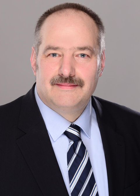 Zwei Männer sitzen in einem Raum. Sie lächeln und scheinen sich gut zu unterhalten.